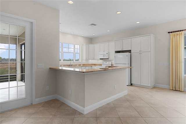 kitchen with kitchen peninsula, white appliances, sink, light tile patterned floors, and white cabinets