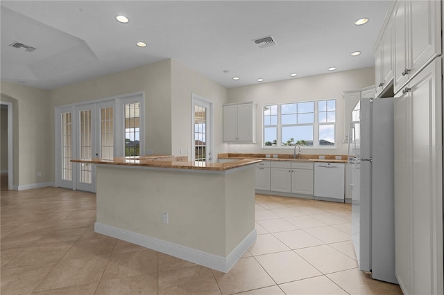 kitchen with white cabinetry, sink, light tile patterned floors, and white appliances