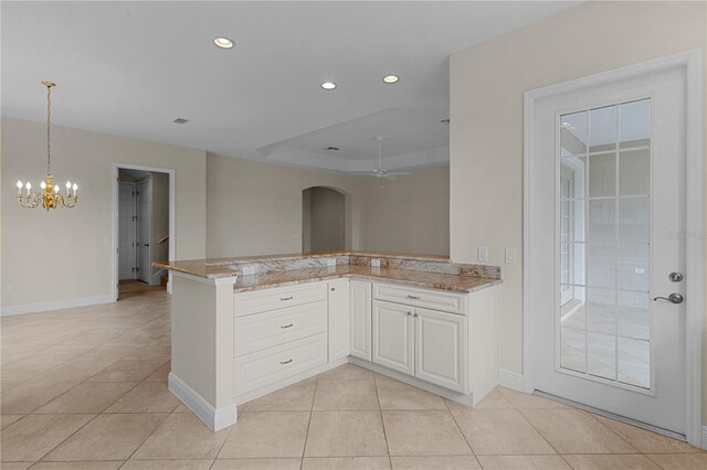 kitchen with white cabinets, kitchen peninsula, a tray ceiling, light tile patterned floors, and ceiling fan with notable chandelier