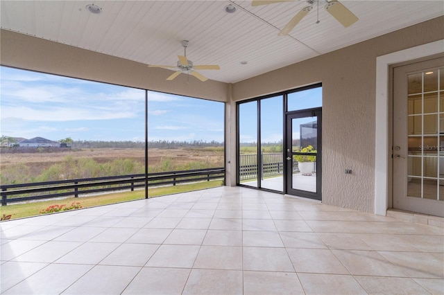 unfurnished sunroom featuring ceiling fan and a rural view