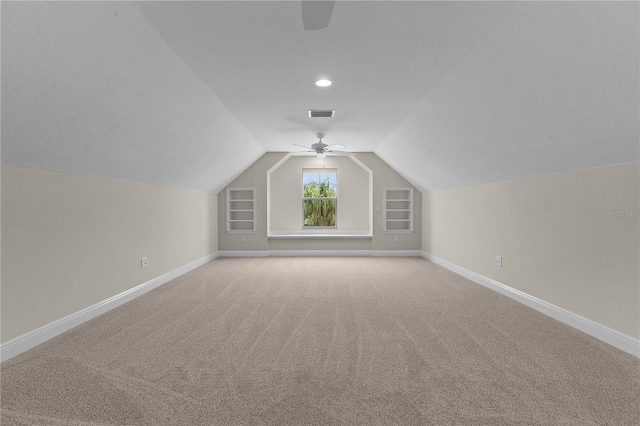 additional living space featuring vaulted ceiling, built in shelves, ceiling fan, a textured ceiling, and light colored carpet