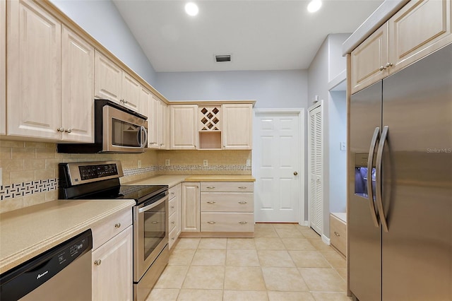 kitchen with tasteful backsplash, light brown cabinets, light tile patterned flooring, and stainless steel appliances