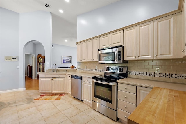 kitchen featuring kitchen peninsula, a high ceiling, appliances with stainless steel finishes, and wooden counters