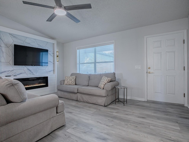 living room featuring ceiling fan, light hardwood / wood-style floors, a textured ceiling, vaulted ceiling, and a fireplace