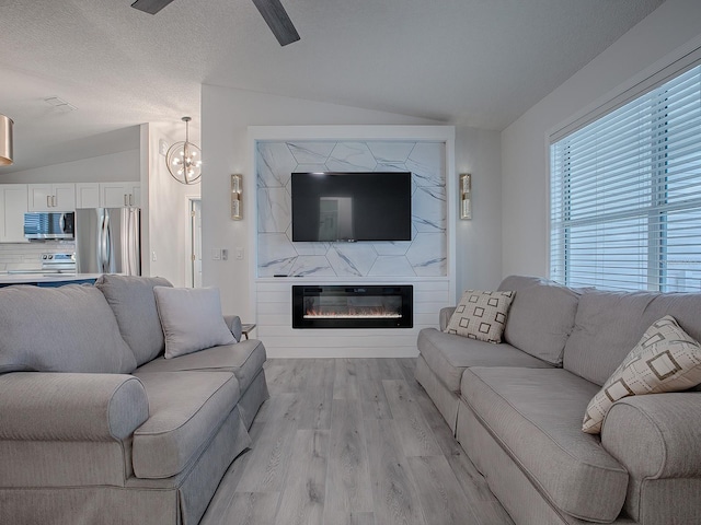 living room with lofted ceiling, light wood-type flooring, a textured ceiling, a large fireplace, and a chandelier