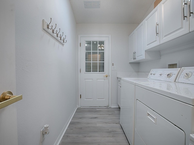 washroom with washer and clothes dryer, cabinets, a textured ceiling, and light wood-type flooring