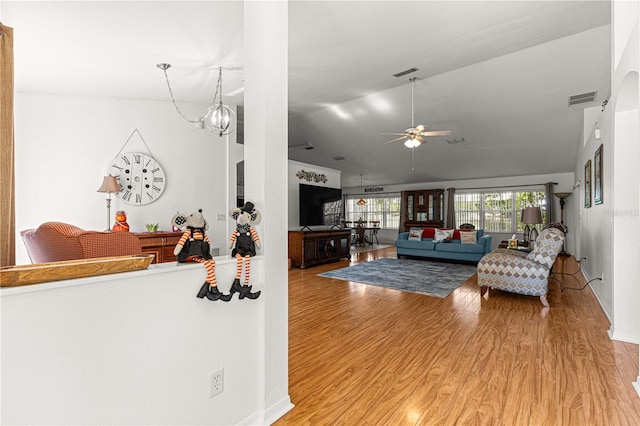 living room with ceiling fan with notable chandelier, light hardwood / wood-style floors, and lofted ceiling