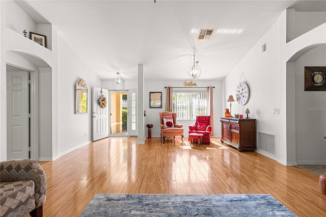 living room with a chandelier, a textured ceiling, and light hardwood / wood-style flooring