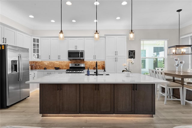 kitchen with white cabinetry, sink, a center island with sink, appliances with stainless steel finishes, and ornamental molding