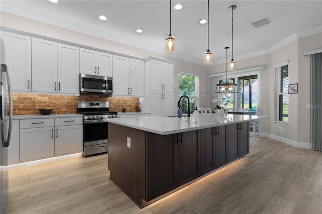 kitchen featuring sink, stainless steel appliances, light hardwood / wood-style floors, decorative light fixtures, and a kitchen island with sink