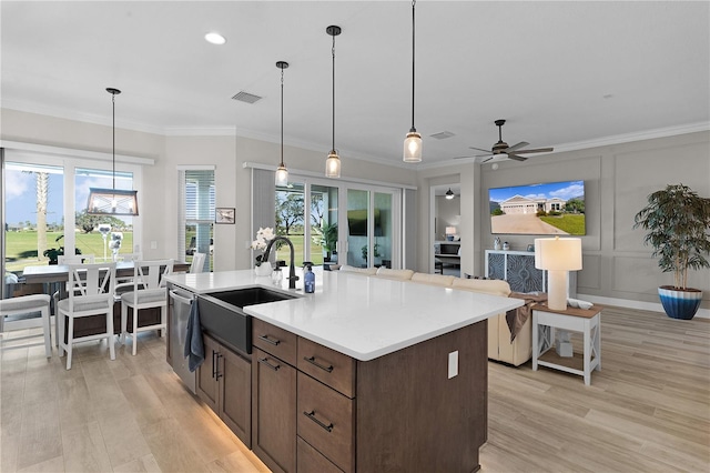 kitchen featuring sink, hanging light fixtures, crown molding, light hardwood / wood-style floors, and a kitchen island with sink