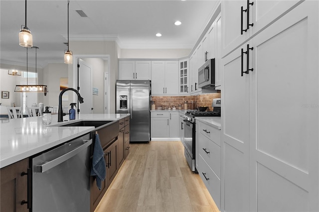 kitchen with pendant lighting, white cabinetry, appliances with stainless steel finishes, and light hardwood / wood-style flooring