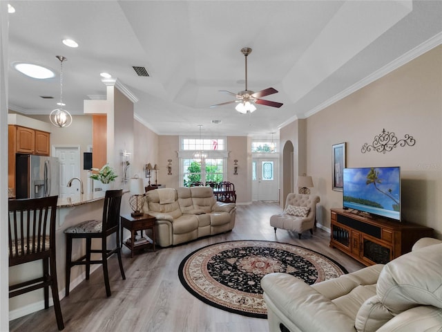 living room with visible vents, arched walkways, light wood-style floors, crown molding, and ceiling fan with notable chandelier