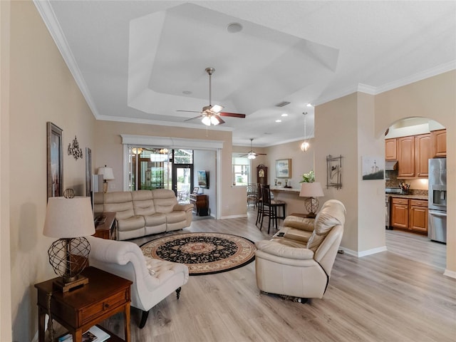 living area with visible vents, light wood-style flooring, a ceiling fan, ornamental molding, and baseboards