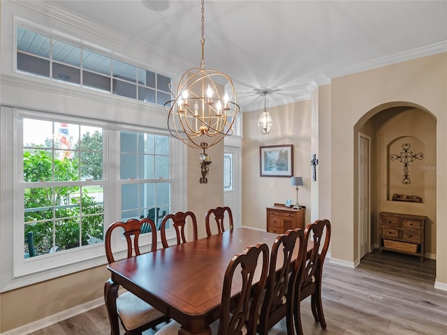 dining area featuring light wood-style flooring, arched walkways, a notable chandelier, and ornamental molding