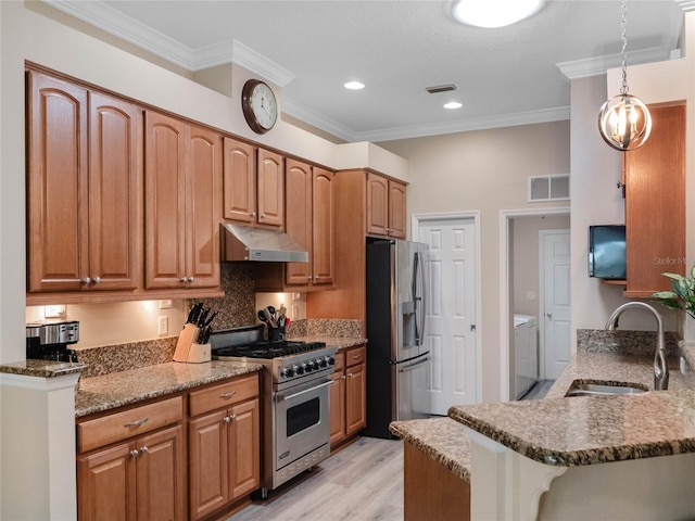 kitchen featuring under cabinet range hood, appliances with stainless steel finishes, washer and dryer, stone countertops, and a sink