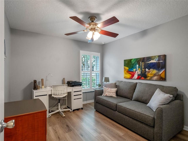 home office featuring ceiling fan, baseboards, a textured ceiling, and light wood-style flooring