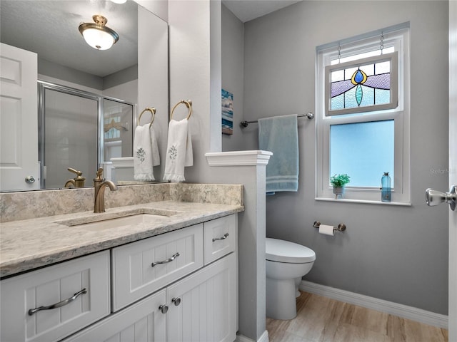 full bathroom featuring toilet, wood finished floors, a shower stall, baseboards, and vanity