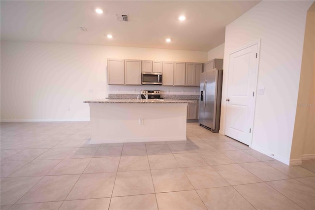 kitchen with a kitchen island with sink, light tile patterned flooring, light stone counters, and appliances with stainless steel finishes