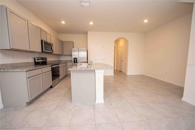 kitchen with light stone countertops, stainless steel appliances, gray cabinetry, and an island with sink