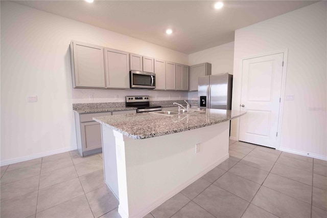 kitchen with light stone countertops, sink, stainless steel appliances, an island with sink, and light tile patterned floors