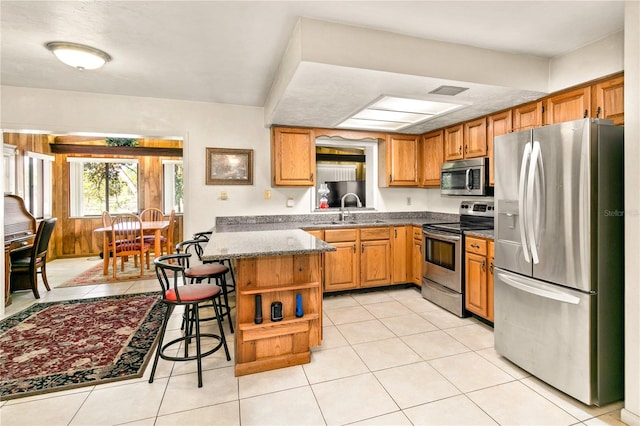 kitchen featuring sink, a kitchen breakfast bar, kitchen peninsula, light tile patterned floors, and appliances with stainless steel finishes