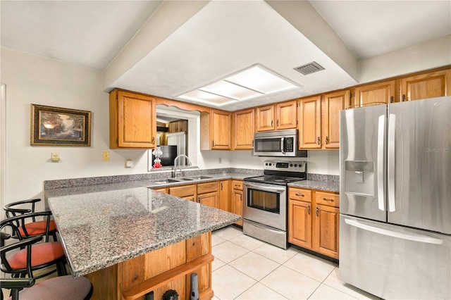 kitchen with a breakfast bar, dark stone counters, sink, appliances with stainless steel finishes, and kitchen peninsula