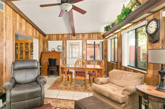 tiled living room with ceiling fan, lofted ceiling with beams, plenty of natural light, and wood walls