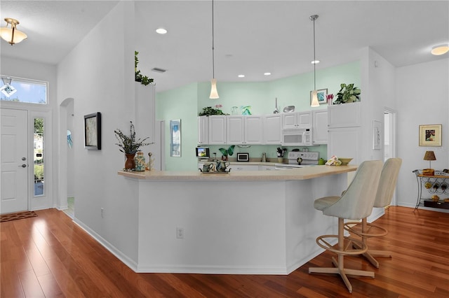 kitchen with white cabinets, pendant lighting, white appliances, and hardwood / wood-style flooring