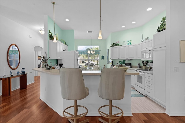 kitchen featuring decorative light fixtures, white appliances, a kitchen bar, white cabinets, and light wood-type flooring