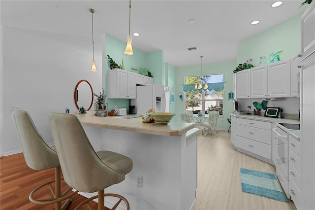 kitchen with a breakfast bar, white appliances, white cabinets, light wood-type flooring, and decorative light fixtures