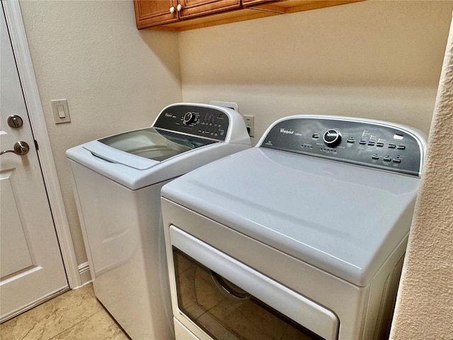 clothes washing area with light tile patterned flooring, cabinets, and washing machine and clothes dryer