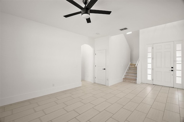 foyer entrance with baseboards, visible vents, arched walkways, a ceiling fan, and stairs