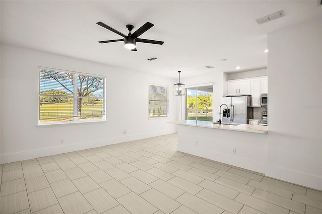 kitchen with white cabinetry, sink, stainless steel appliances, pendant lighting, and ceiling fan with notable chandelier