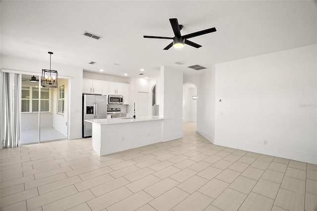 kitchen with kitchen peninsula, ceiling fan with notable chandelier, stainless steel appliances, pendant lighting, and white cabinets