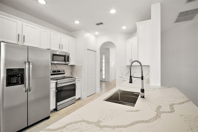 kitchen with backsplash, light stone counters, white cabinets, and stainless steel appliances