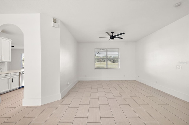 unfurnished room featuring a healthy amount of sunlight, baseboards, arched walkways, and a ceiling fan