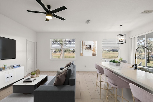 living area with ceiling fan with notable chandelier, a wealth of natural light, and visible vents