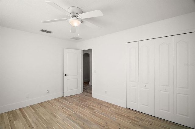 unfurnished bedroom featuring arched walkways, light wood finished floors, a closet, and baseboards