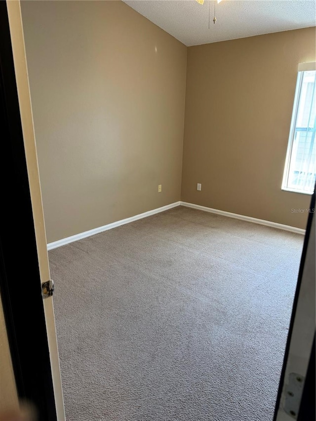 carpeted spare room with a textured ceiling and baseboards