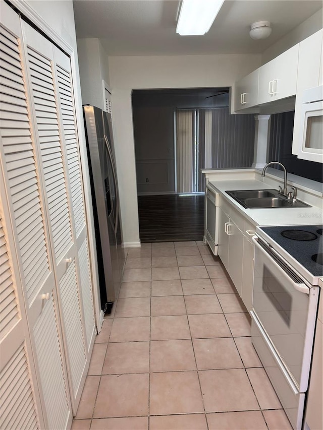 kitchen with light tile patterned floors, light countertops, white cabinets, a sink, and white appliances