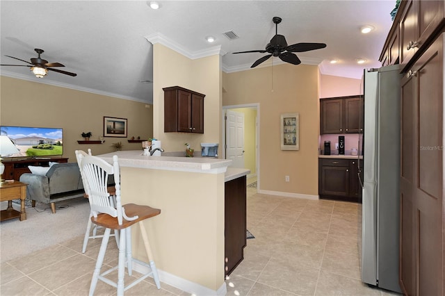 kitchen with a breakfast bar area, stainless steel refrigerator, ceiling fan, and ornamental molding