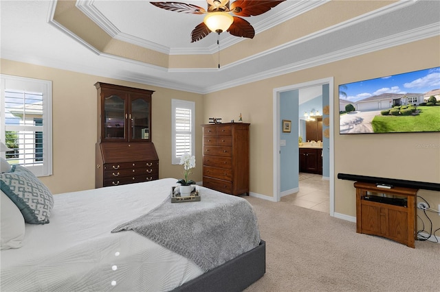 carpeted bedroom featuring a tray ceiling, connected bathroom, ceiling fan, and ornamental molding