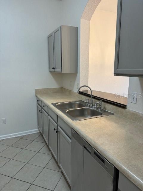 kitchen with light tile patterned floors, gray cabinets, stainless steel dishwasher, and sink