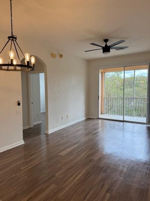 empty room featuring ceiling fan with notable chandelier and dark hardwood / wood-style floors