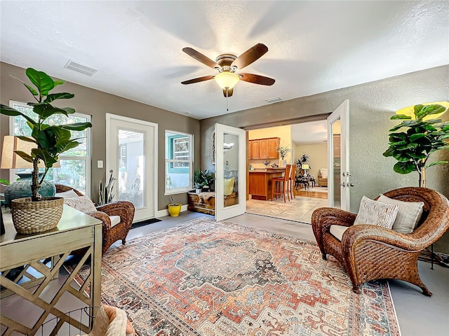 living area featuring ceiling fan, french doors, a healthy amount of sunlight, and a textured ceiling