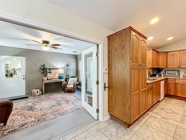 kitchen featuring white dishwasher, sink, vaulted ceiling, ceiling fan, and a textured ceiling