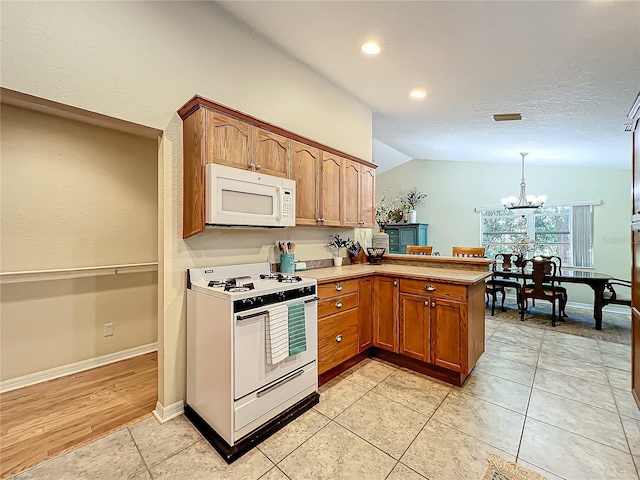 kitchen with kitchen peninsula, white appliances, decorative light fixtures, a chandelier, and lofted ceiling