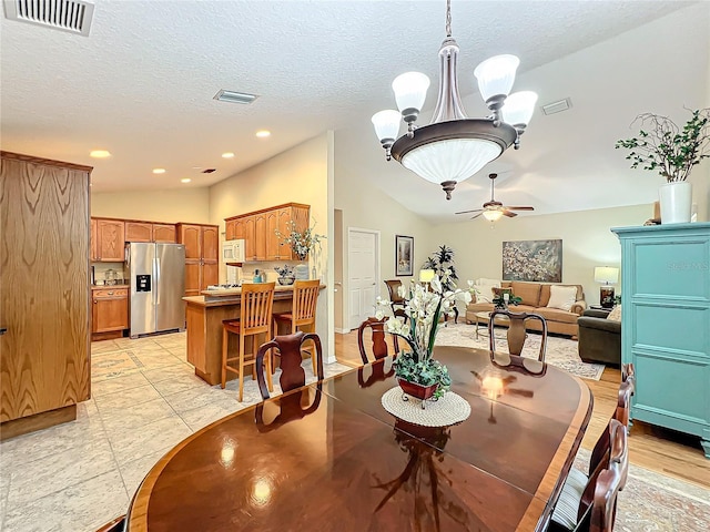 tiled dining space featuring a textured ceiling, ceiling fan with notable chandelier, and vaulted ceiling