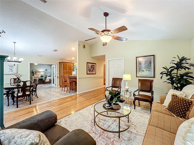 living room featuring a textured ceiling, ceiling fan with notable chandelier, light hardwood / wood-style floors, and vaulted ceiling